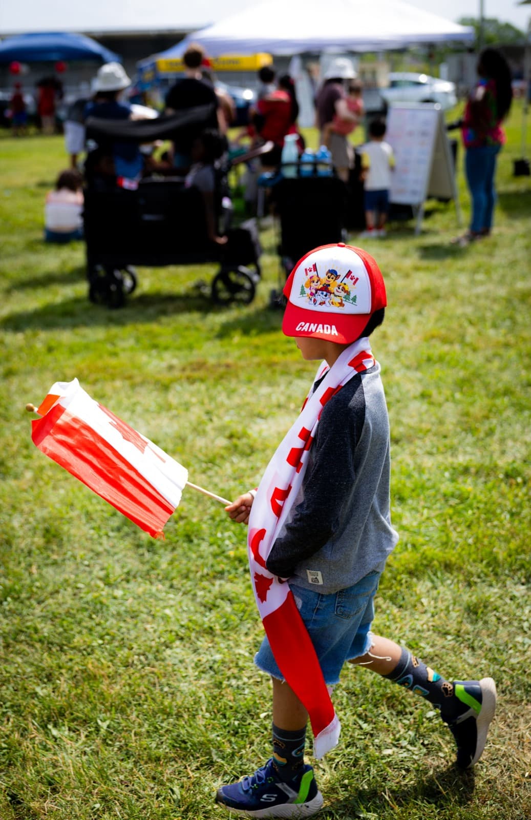 A kid carrying the Canadian flag across the field on Canada Day